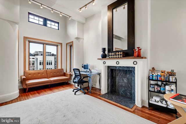 office area featuring rail lighting, a high ceiling, a high end fireplace, and hardwood / wood-style flooring