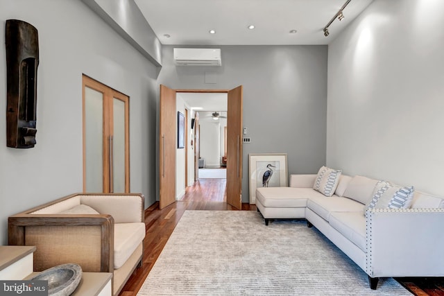 living room with track lighting, hardwood / wood-style floors, an AC wall unit, and a high ceiling