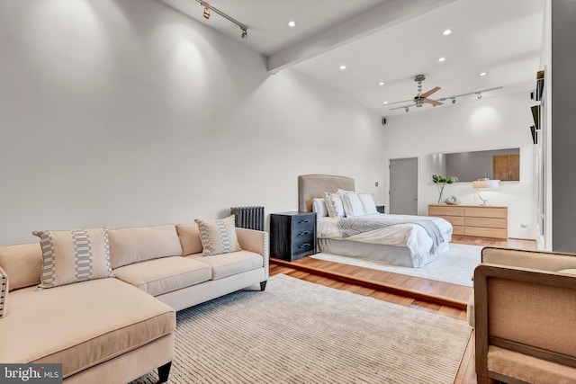 bedroom with track lighting, beamed ceiling, radiator heating unit, ceiling fan, and hardwood / wood-style flooring