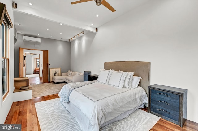 bedroom with a wall mounted AC, ceiling fan, beamed ceiling, and light wood-type flooring