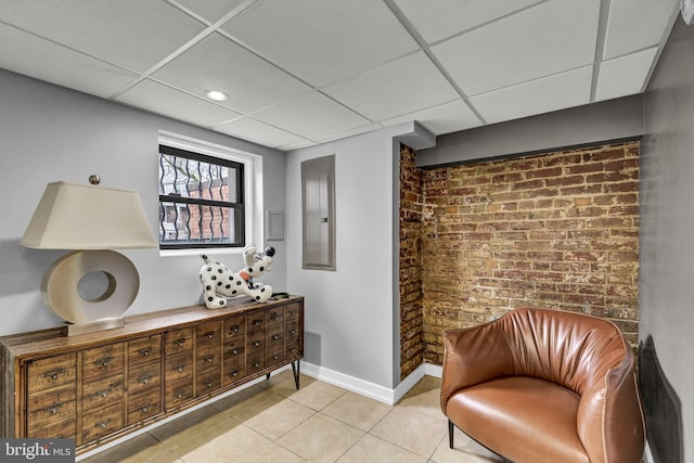 living area with a paneled ceiling, electric panel, brick wall, and light tile patterned flooring