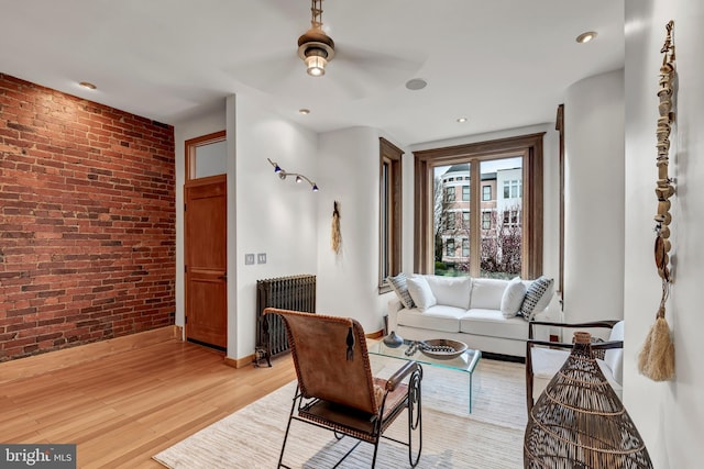 living room featuring light hardwood / wood-style flooring, ceiling fan, radiator heating unit, and brick wall