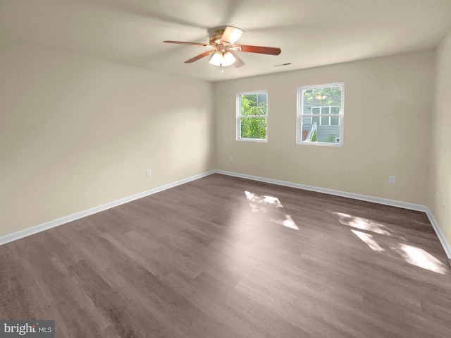 empty room featuring dark wood-type flooring, visible vents, ceiling fan, and baseboards