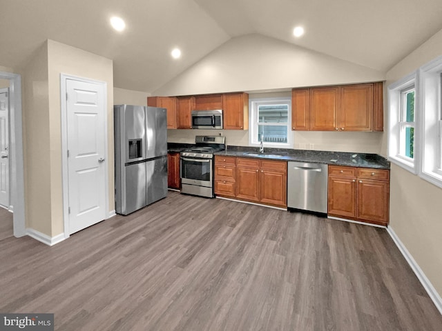 kitchen with brown cabinets, stainless steel appliances, dark countertops, dark wood-type flooring, and a sink