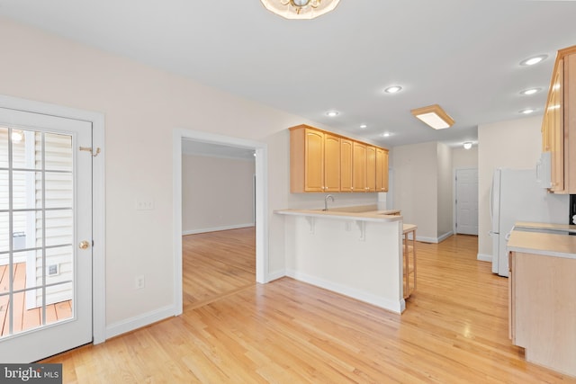 kitchen featuring light hardwood / wood-style floors, a kitchen bar, kitchen peninsula, and light brown cabinets