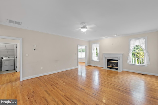 unfurnished living room featuring light wood-type flooring, washer / dryer, a wealth of natural light, a high end fireplace, and ceiling fan