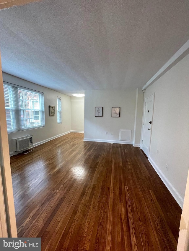 unfurnished living room featuring a textured ceiling, an AC wall unit, and dark hardwood / wood-style flooring