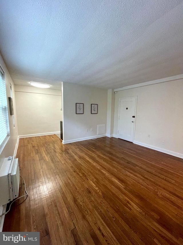 empty room featuring an AC wall unit, a textured ceiling, and dark hardwood / wood-style flooring