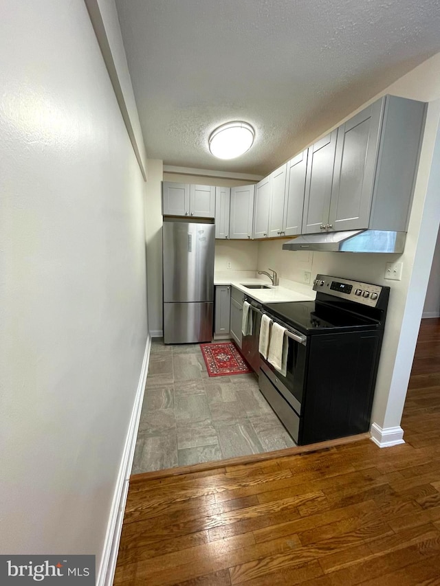 kitchen featuring a textured ceiling, light wood-type flooring, sink, gray cabinetry, and stainless steel appliances