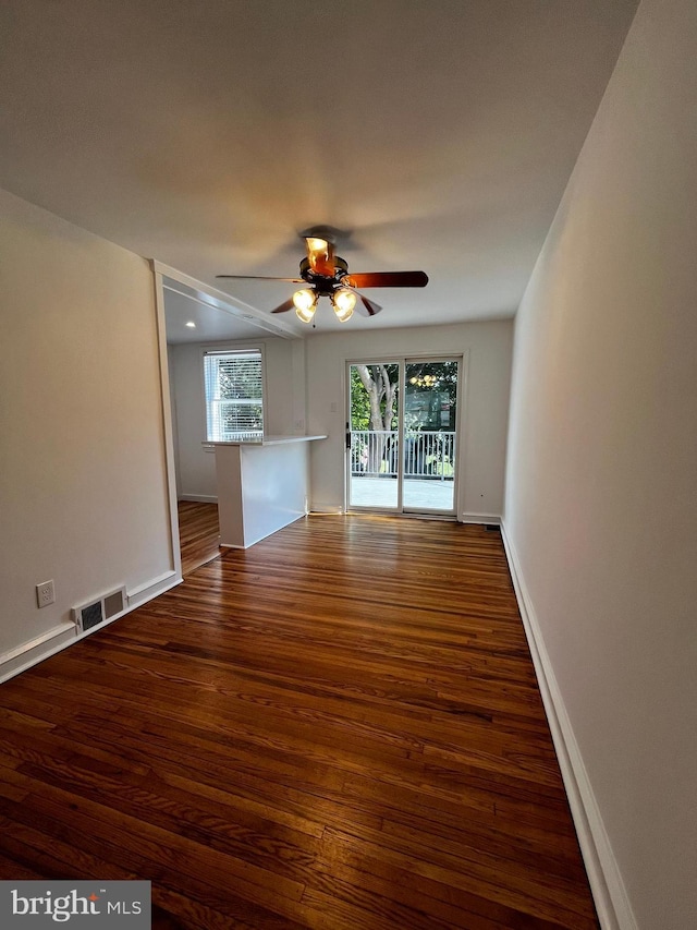 empty room with dark wood-style floors, ceiling fan, visible vents, and baseboards