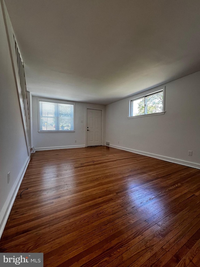 unfurnished room featuring plenty of natural light, visible vents, baseboards, and dark wood-type flooring