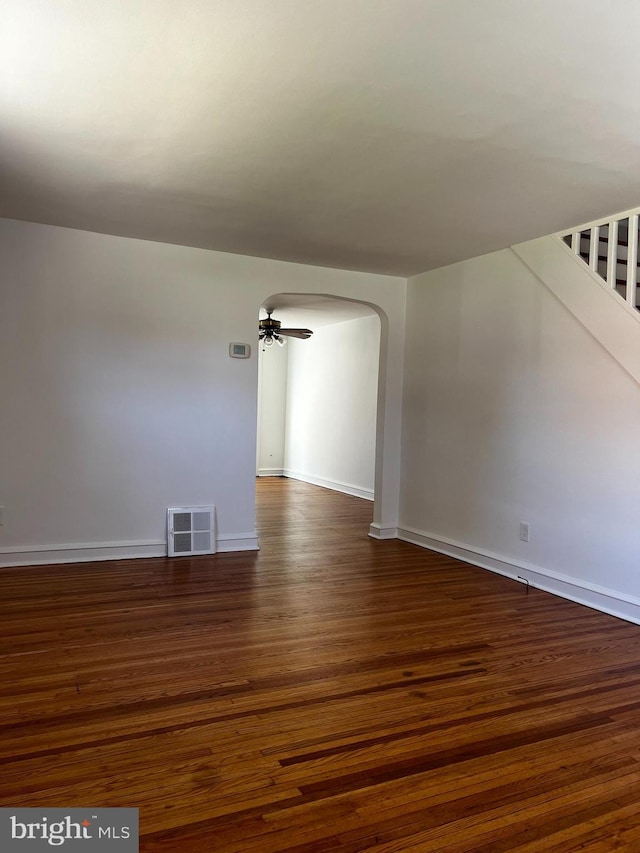 empty room featuring arched walkways, dark wood-type flooring, visible vents, a ceiling fan, and stairs