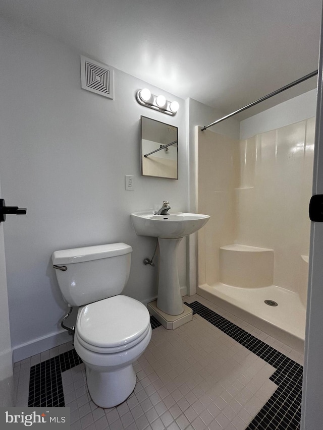 bathroom with toilet, a shower, and tile patterned floors