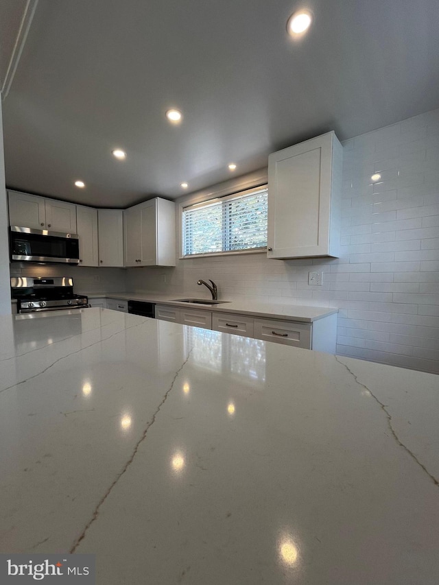 kitchen featuring sink, white cabinetry, stove, and light stone countertops