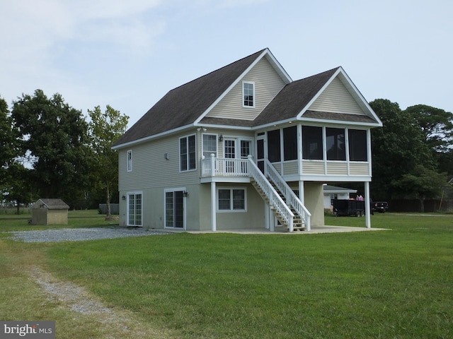 rear view of property with a shingled roof, a sunroom, stairs, a yard, and stucco siding