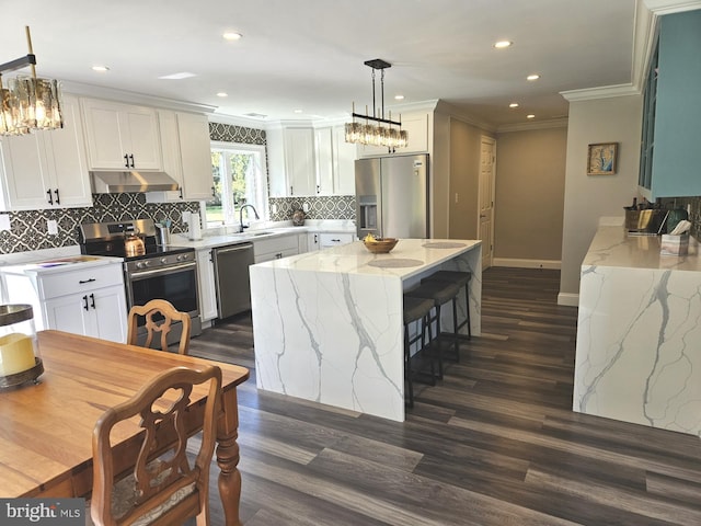 kitchen with hanging light fixtures, under cabinet range hood, white cabinetry, and appliances with stainless steel finishes