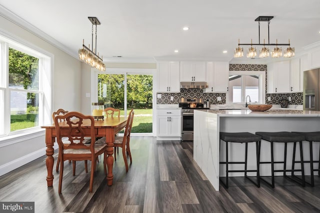 kitchen with white cabinets, stainless steel appliances, crown molding, and decorative light fixtures