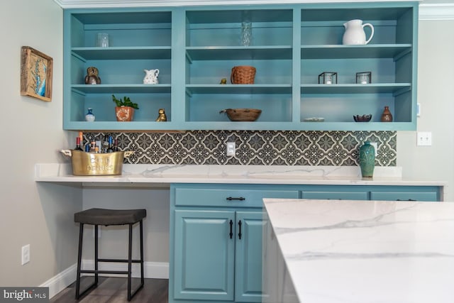 bar with light stone countertops, blue cabinets, dark hardwood / wood-style flooring, and backsplash