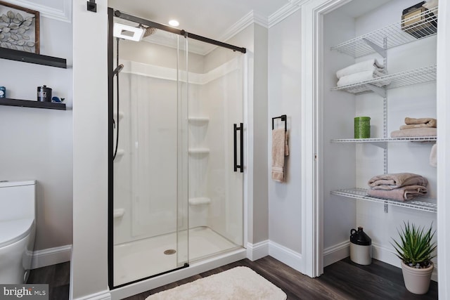 full bathroom with toilet, wood finished floors, baseboards, a shower stall, and crown molding