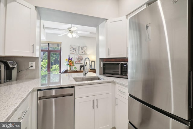 kitchen with white cabinets, appliances with stainless steel finishes, a sink, light stone countertops, and backsplash