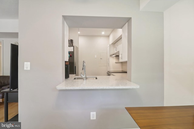 kitchen with sink, light stone counters, white cabinetry, and hardwood / wood-style flooring