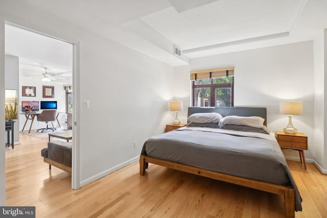 bedroom with light hardwood / wood-style flooring, ceiling fan, and a raised ceiling