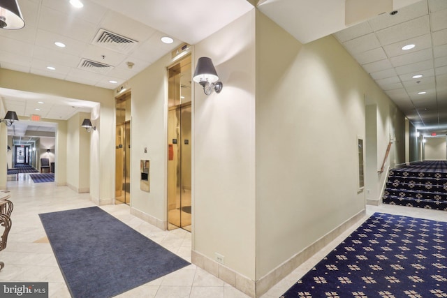 hallway featuring light tile patterned flooring, a drop ceiling, and elevator