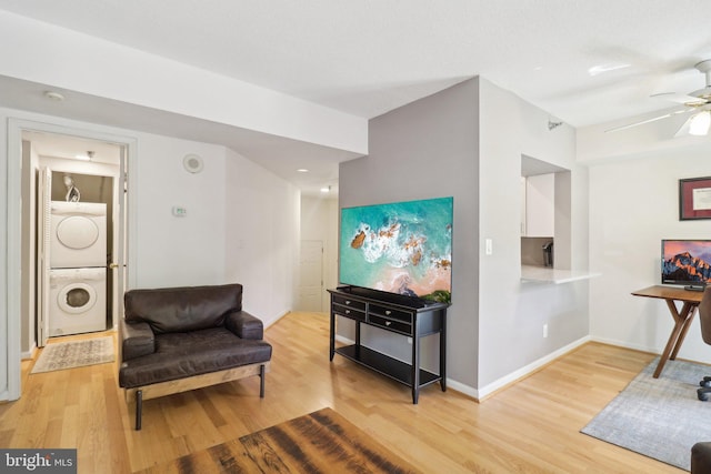 living area with stacked washing maching and dryer, light wood-style flooring, baseboards, and ceiling fan