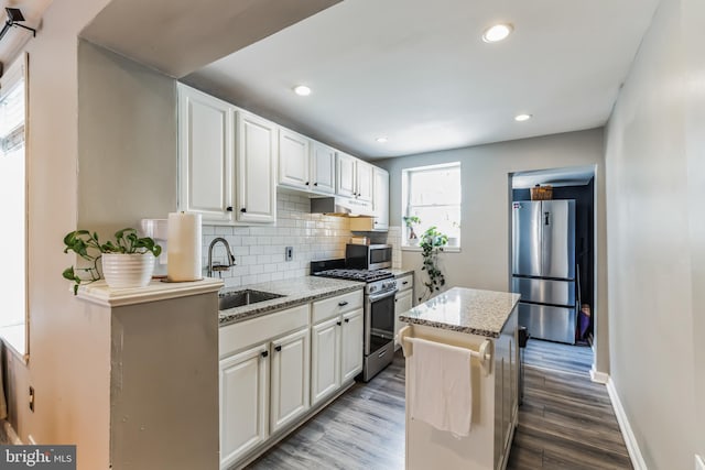 kitchen featuring a kitchen island, appliances with stainless steel finishes, light stone countertops, white cabinetry, and a sink