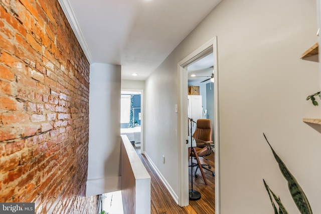 hallway featuring baseboards, brick wall, and wood finished floors