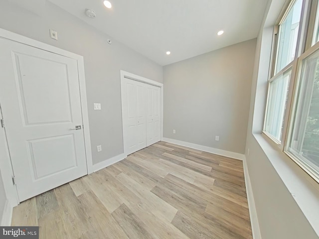 unfurnished bedroom featuring light hardwood / wood-style flooring, multiple windows, and a closet