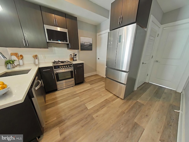 kitchen featuring stainless steel appliances, backsplash, sink, dark brown cabinetry, and light wood-type flooring