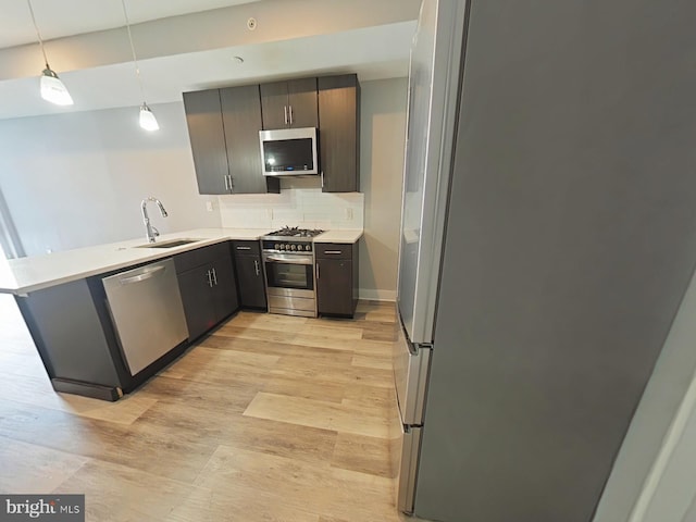 kitchen featuring appliances with stainless steel finishes, sink, kitchen peninsula, light hardwood / wood-style floors, and pendant lighting