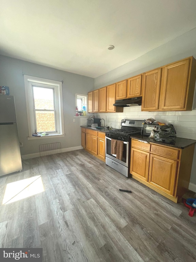 kitchen featuring backsplash, radiator, appliances with stainless steel finishes, and hardwood / wood-style flooring