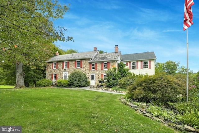 view of front of house featuring stone siding, a front lawn, and a chimney