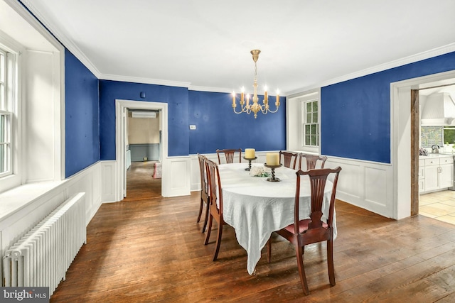 dining area featuring dark wood-style floors, a wainscoted wall, radiator heating unit, an inviting chandelier, and ornamental molding