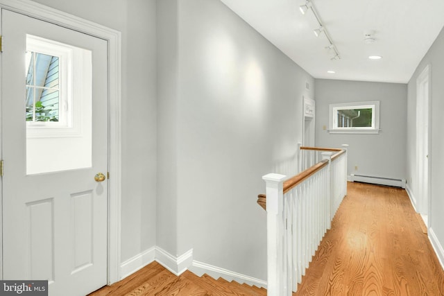 hallway with lofted ceiling, an upstairs landing, light wood-style floors, a baseboard heating unit, and track lighting