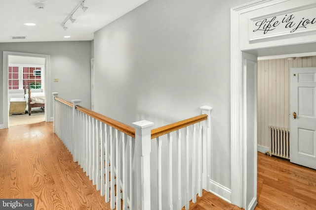 corridor featuring visible vents, light wood-style flooring, radiator heating unit, and an upstairs landing