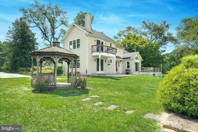 back of house with a balcony, a yard, a chimney, and a gazebo