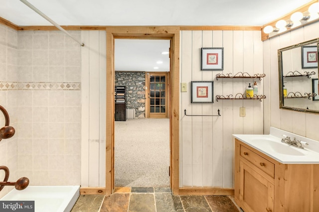 bathroom with stone finish flooring, tiled shower, and vanity