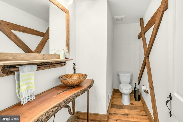 bathroom featuring toilet, wood finished floors, a sink, visible vents, and baseboards