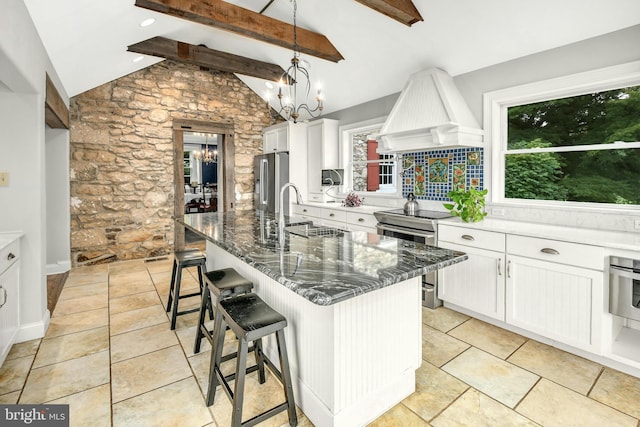 kitchen featuring a center island with sink, appliances with stainless steel finishes, a sink, a chandelier, and premium range hood