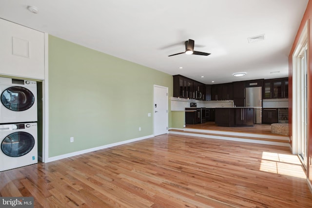 unfurnished living room featuring ceiling fan, stacked washer / drying machine, and light wood-type flooring