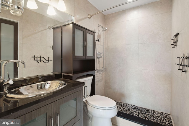 bathroom featuring toilet, a tile shower, vanity, and tile walls