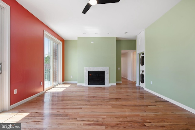 unfurnished living room featuring ceiling fan, light wood-type flooring, and stacked washing maching and dryer