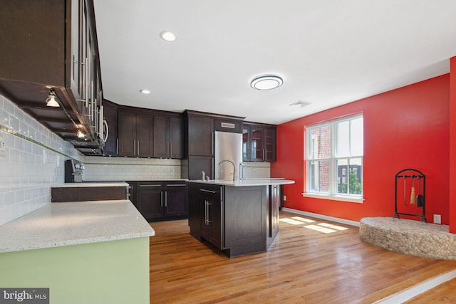 kitchen featuring decorative backsplash, an island with sink, light hardwood / wood-style floors, stainless steel fridge, and range with electric stovetop