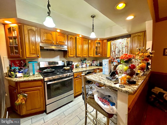 kitchen with decorative backsplash, a raised ceiling, hanging light fixtures, stainless steel range with gas stovetop, and light stone countertops