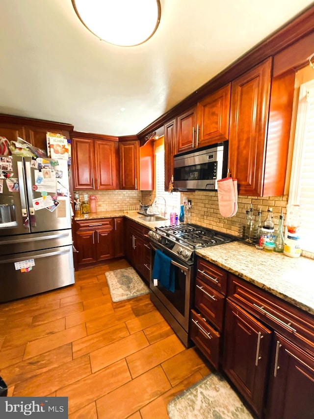 kitchen with appliances with stainless steel finishes, light stone countertops, tasteful backsplash, and light wood-type flooring