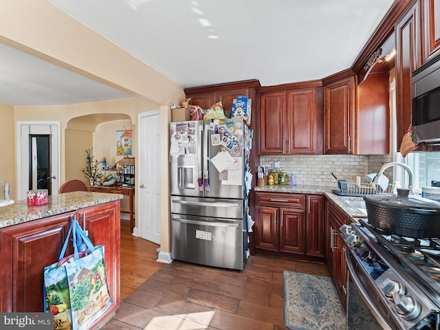 kitchen with tasteful backsplash, appliances with stainless steel finishes, dark wood-type flooring, sink, and light stone counters