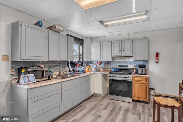 kitchen with appliances with stainless steel finishes, light hardwood / wood-style flooring, tasteful backsplash, a paneled ceiling, and gray cabinetry